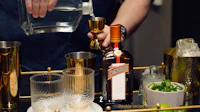 a person pouring a drink from a bottle on a gold tray